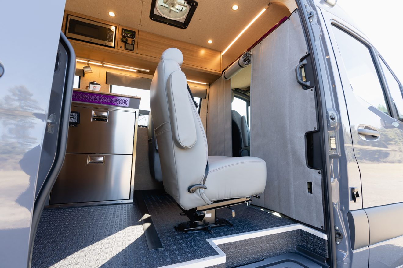 Open passenger slider door with side step next to two travel approved captain's chairs in front of an insulated soft garage wall