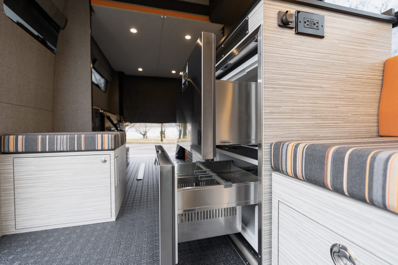 Interior with custom orange and grey striped upholstery next to vitrifrigro stainless steel refrigerator bench seat with dual pullout storage drawers
