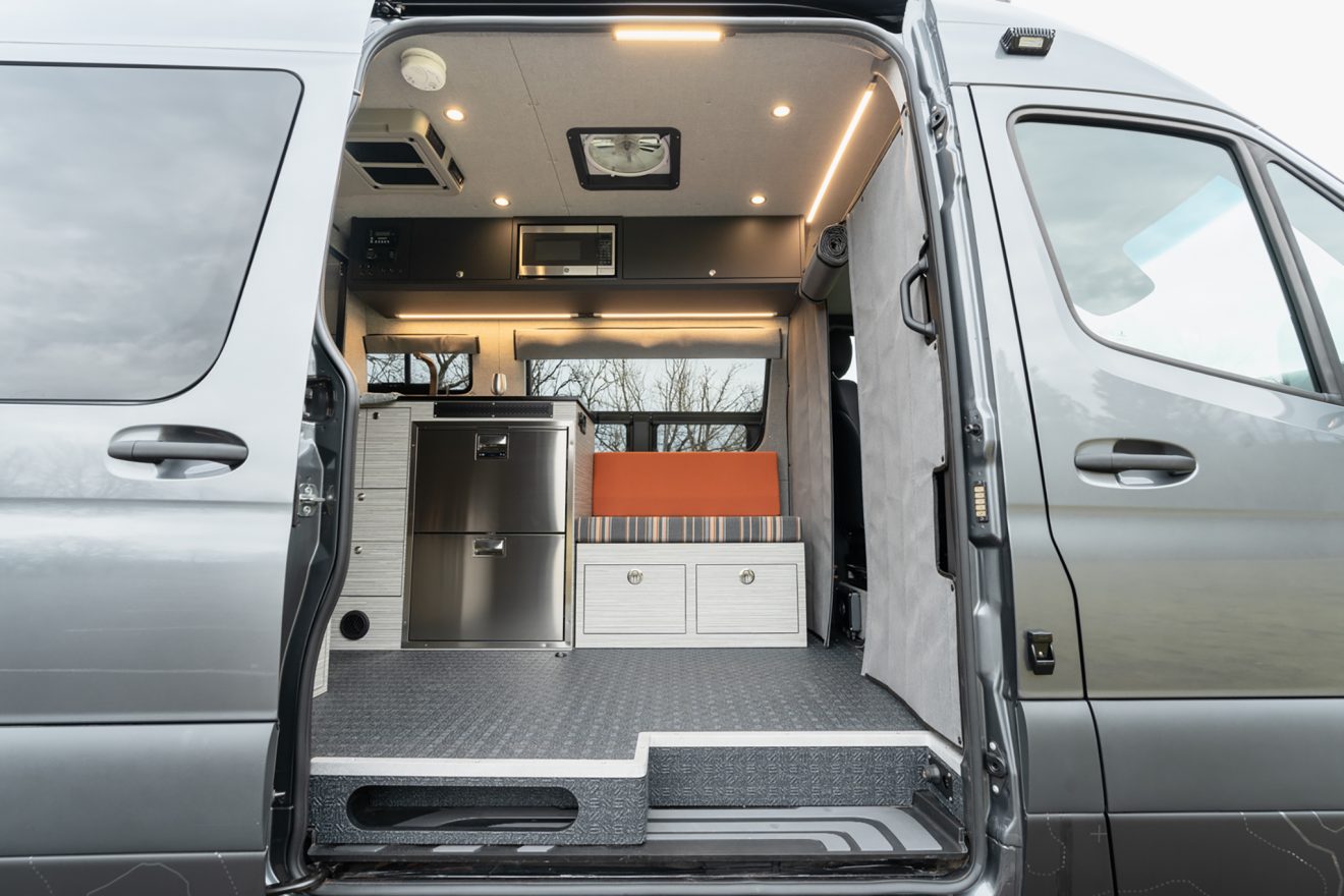 Van cabin interior with custom orange and grey striped upholstery next to vitrifrigro stainless steel refrigerator