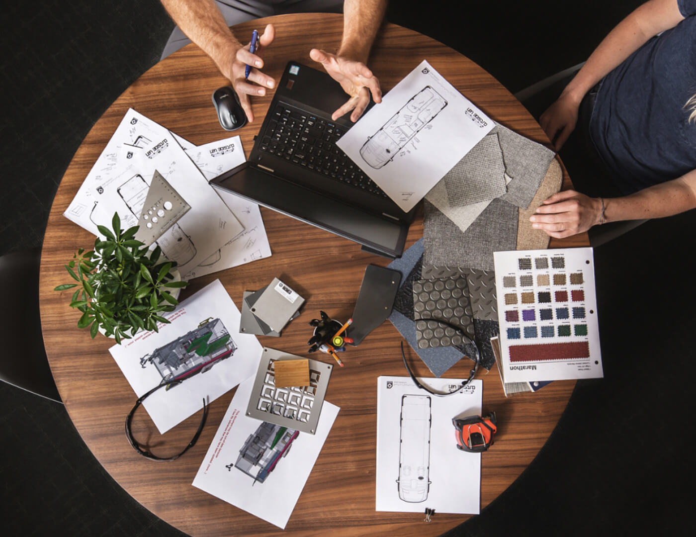 Top down view of table with people working and various work items on the desk.